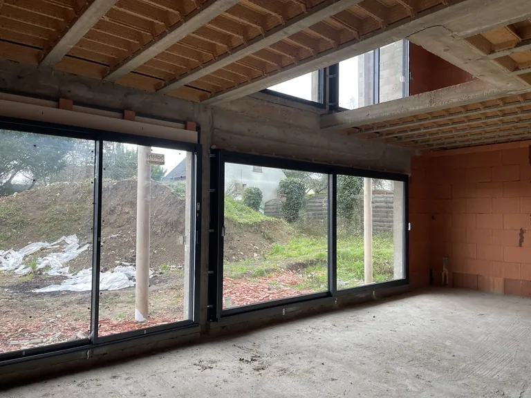 Grandes baies vitrées dans un bâtiment en chantier avec murs en briques et plancher apparent