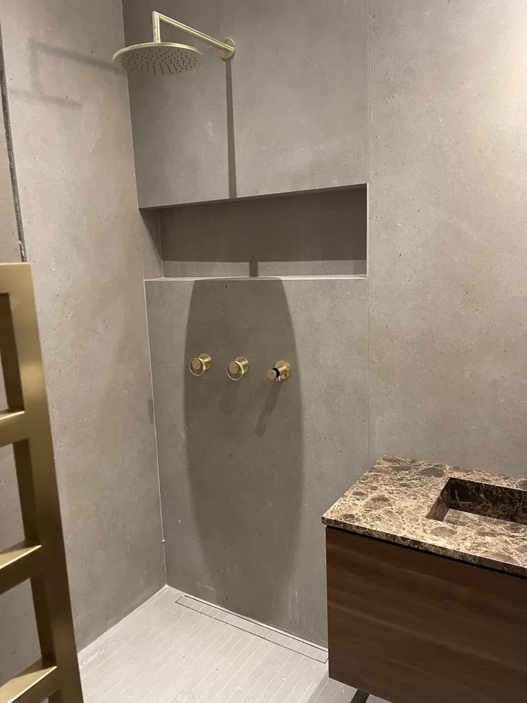 Salle de bain avec douche carrelée, niche, robinetterie laiton et vasque veinée sur meuble bois